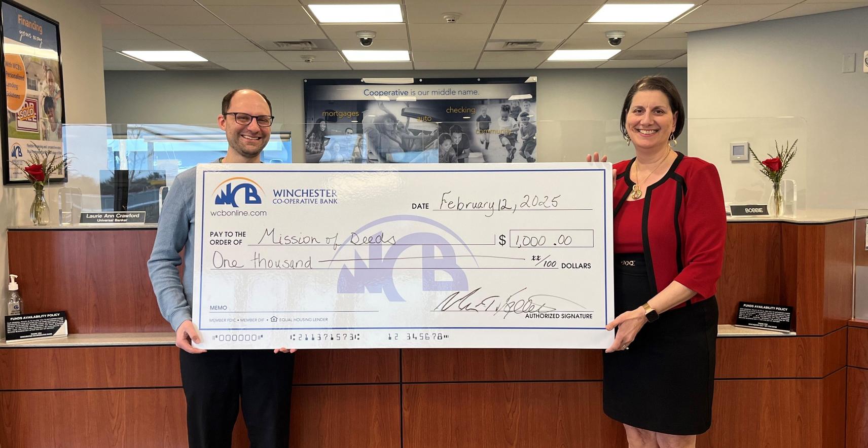 a man and a woman holding the big donation check made out to the Mission of Deeds