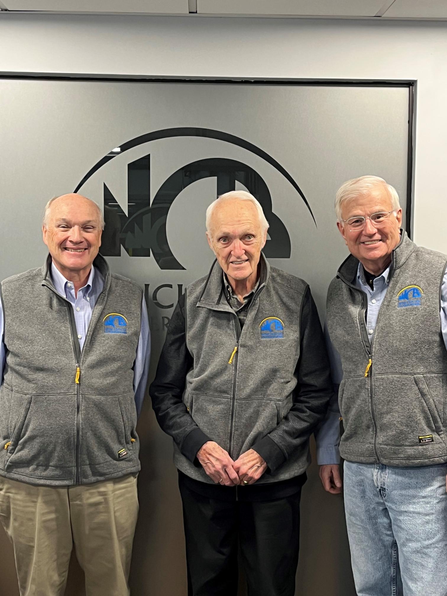 Three gentlemen in front of WCB sign